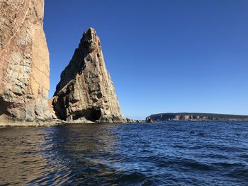 Rock formation in sea against clear blue sky