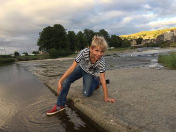 Portrait of boy stepping on puddle against cloudy sky