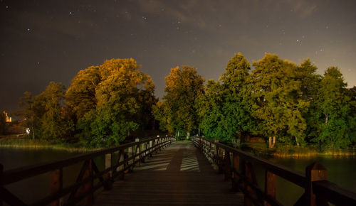 Footpath amidst trees against sky at night