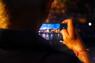 Rear view of man photographing through mobile phone at night