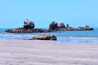 Rocks on beach against clear blue sky