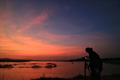 Silhouette man standing by lake against sky during sunset