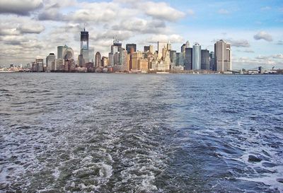 Sea by modern buildings in city against sky