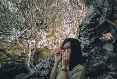 Portrait of woman holding sunglases against plants