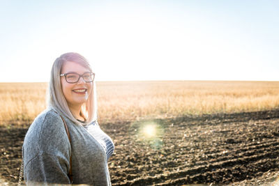 Portrait of smiling young woman on field against sky