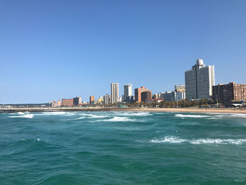 Sea by buildings against clear sky