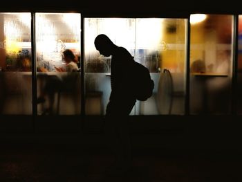 Silhouette people looking through window at night