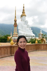 Portrait of woman standing against buddha statues