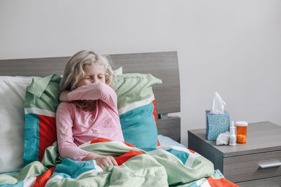 Sick ill kid girl with fever lying in bed at home with flu, fever and sneezing in elbow