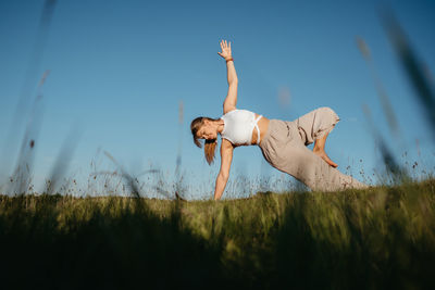 Young woman practicing yoga outdoors in the field with blue sky on the background	
