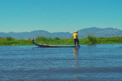 Man in boat sailing on water against clear sky