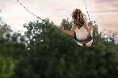 Rear view of girl swinging against trees