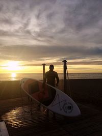 Man on boat at beach against sky during sunset