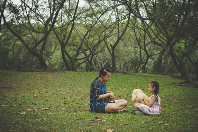 Side view of mother with daughter sitting on grassy field in park