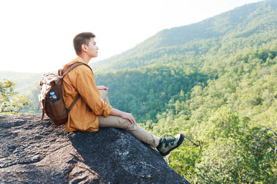 Young man sitting on mountain against trees