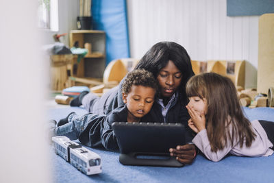 Child care worker sharing digital tablet with students in kindergarten