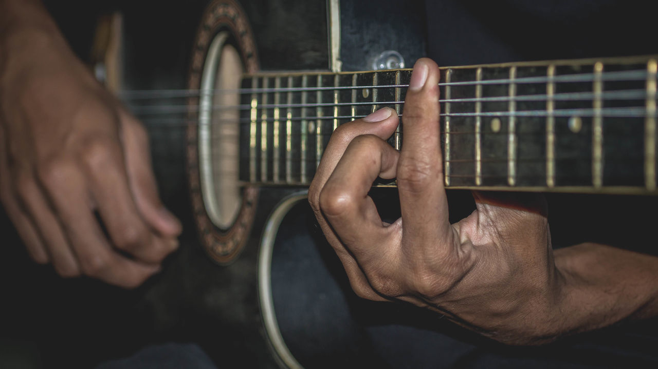 MIDSECTION OF MAN PLAYING GUITAR AT MUSIC