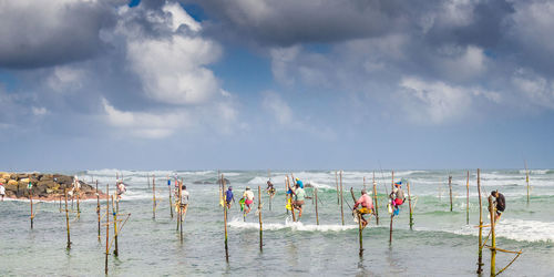 Men fishing in sea against cloudy sky