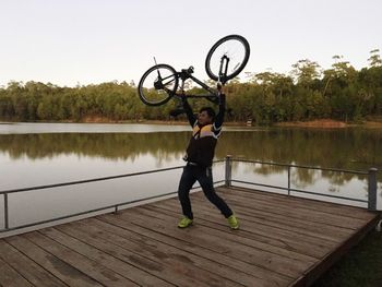 Rear view of man with bicycle on lake against sky