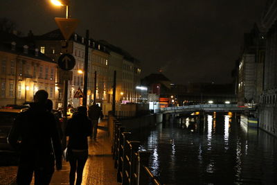 People on illuminated street by buildings at night