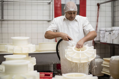 Cheese factory worker cleaning containers with hose