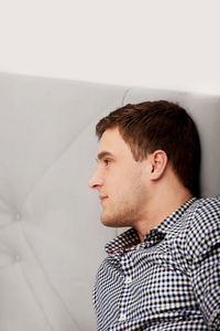 Portrait of young man looking away against wall at home