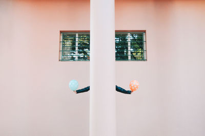 Person holding balloons while hiding behind column