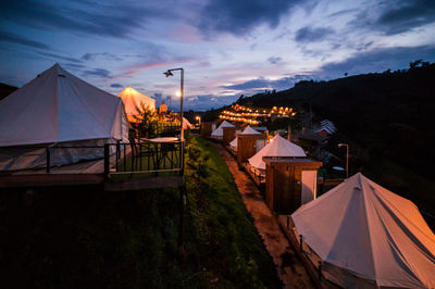 Tent by illuminated buildings against sky at sunset