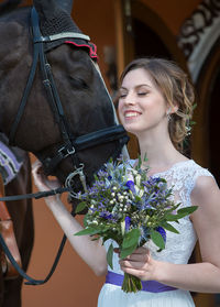 Smiling beautiful bride holding flower bouquet by brown horse