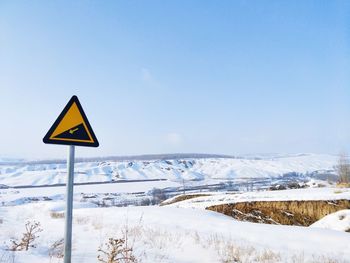 Road sign on snow covered land against sky