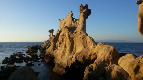 Rock formation in sea against clear sky