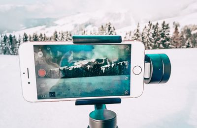 Close-up of mobile phone photographing snowcapped mountains