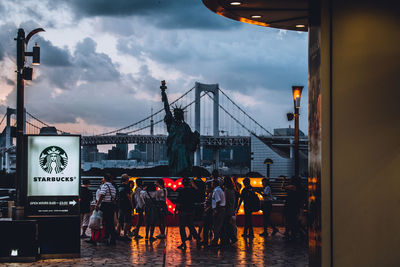 People on bridge in city against sky at sunset