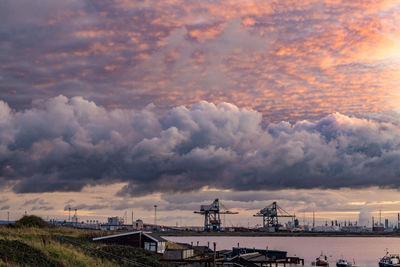 Cranes on pier against sky at sunset