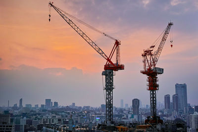 Cranes at construction site in city against sky during sunset