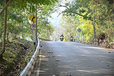 People riding motorcycle on road amidst trees