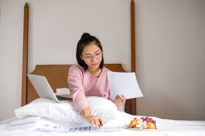 Young woman using phone while sitting on bed