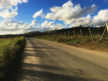 Empty road amidst field against sky