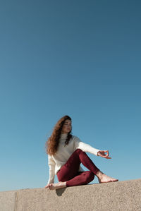 Woman sitting on street against clear blue sky