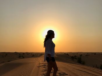 Woman standing on desert during sunset