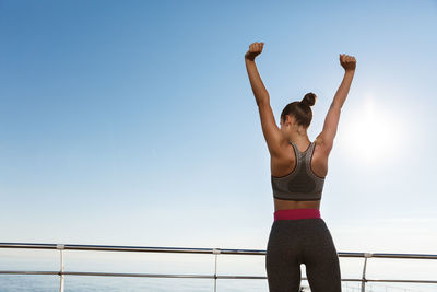 Woman exercising while standing against sea and sky