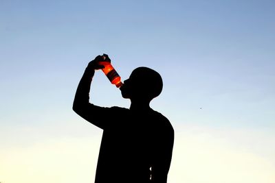 Silhouette man photographing camera against clear sky