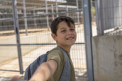 Portrait of smiling boy standing by fence in schoolyard