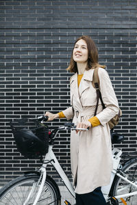 Smiling woman with e-bike at a brick wall