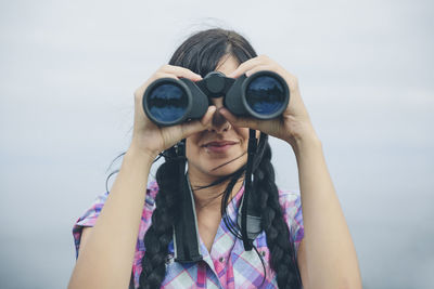 Portrait of young woman holding sunglasses against sky