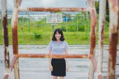 Portrait of smiling young woman seen through metallic outdoor play equipment during rainy season 