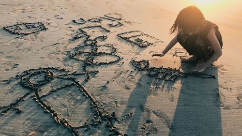 Full length of girl drawing in sand on shore at beach during sunset