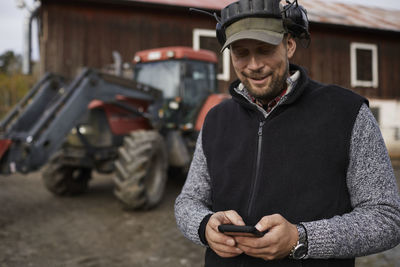 Farmer with cell phone standing next to tractor
