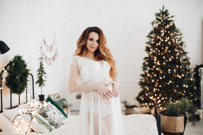 Portrait of young woman standing against christmas tree