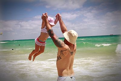 Shirtless father playing with daughter at beach